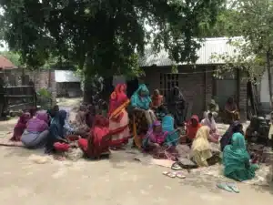 Women in colourful saris sit together outdoors at a community gathering