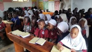 Children in school uniforms and hijabs read from books at their desks