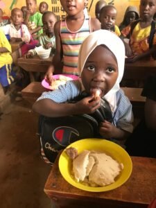 A girl in a white hijab eats her school lunch with a plate of food in front of her